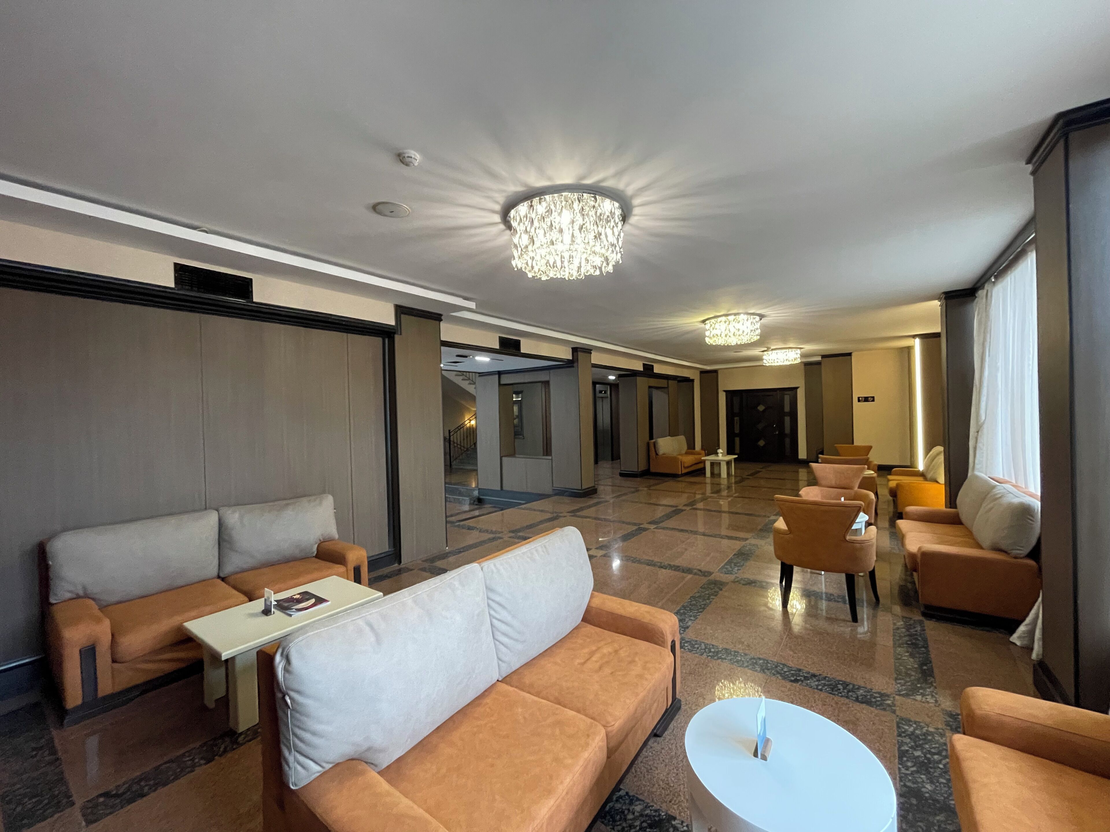 A hotel lobby with a seating area, a chandelier, and a view of the hallway.