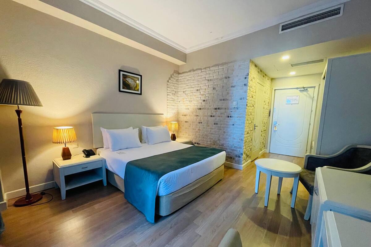 A hotel room with a bed, bedside lamps, a desk, a chair, and a door leading to a bathroom.