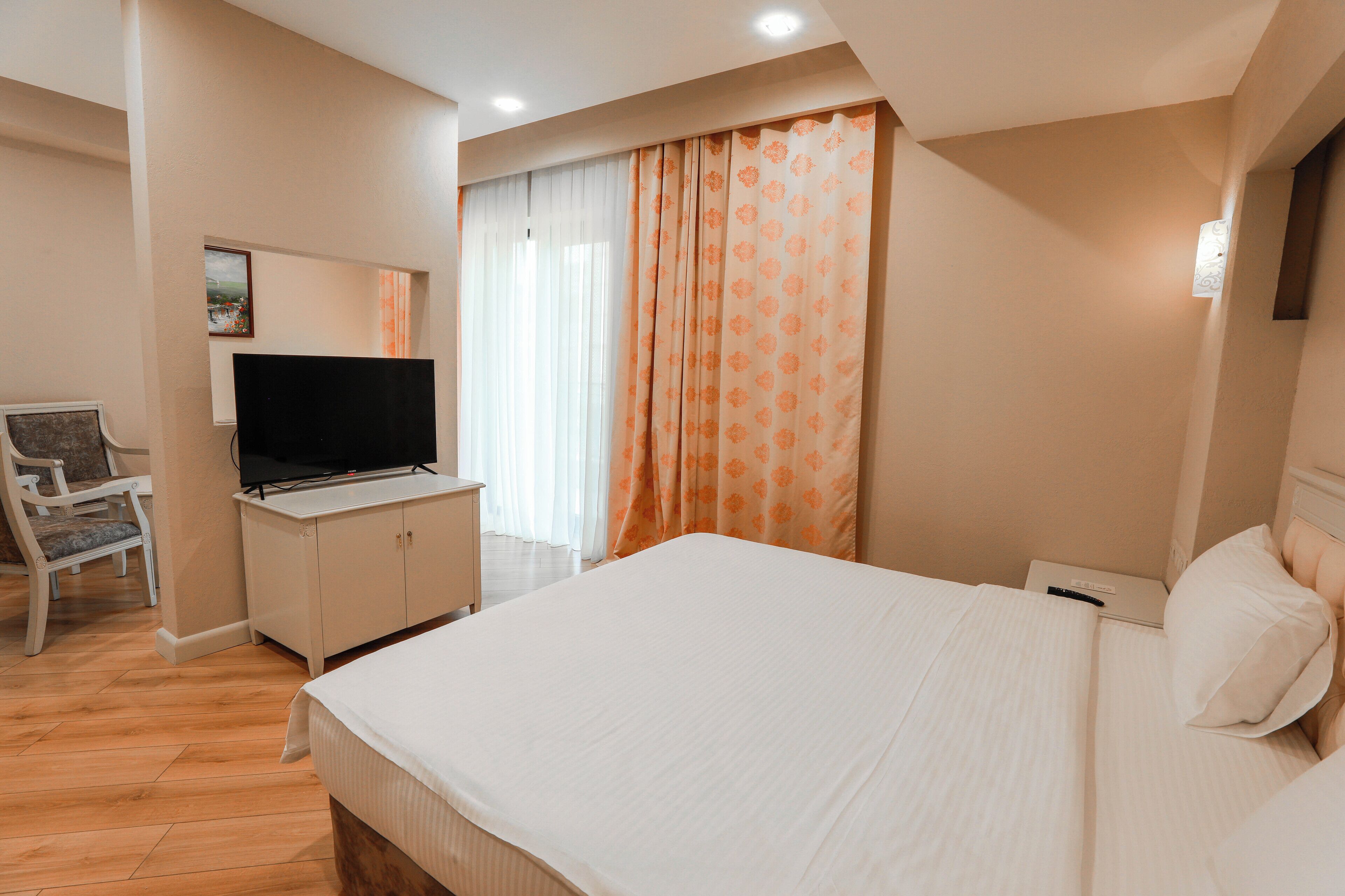 A hotel room with a large bed, a desk with a television, a chair, and a window with curtains.