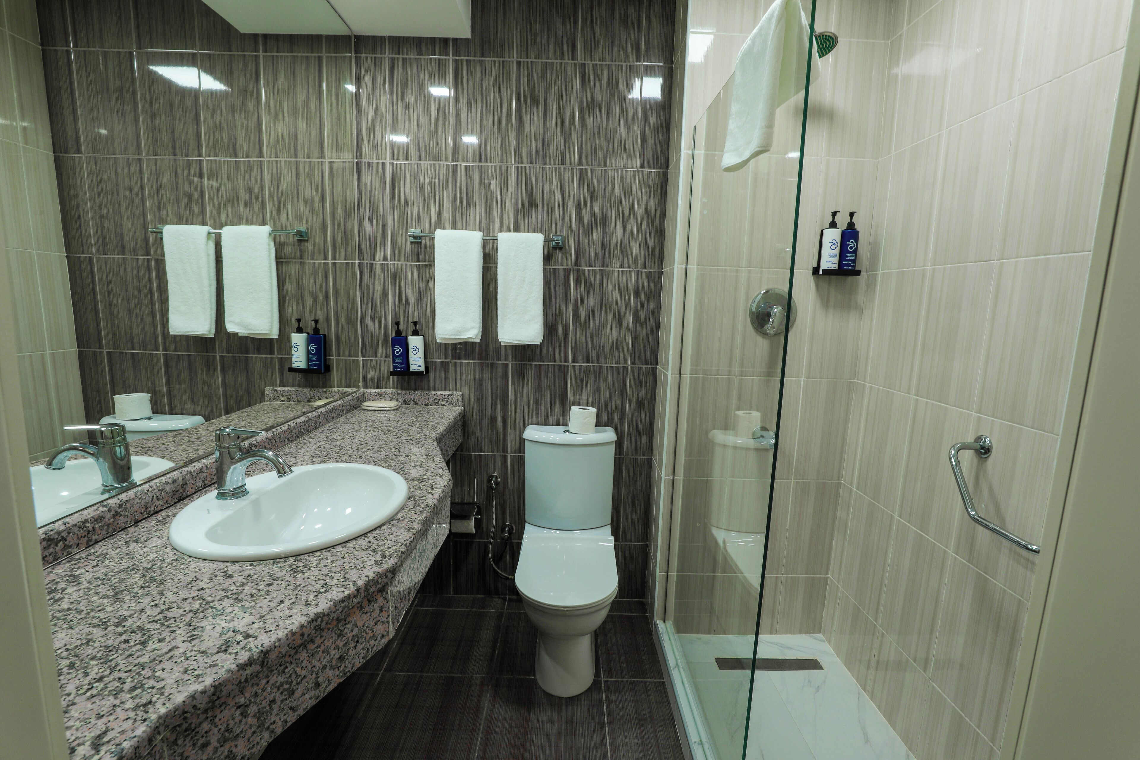 Une salle de bain moderne avec deux lavabos, des toilettes et une douche à parois de verre.