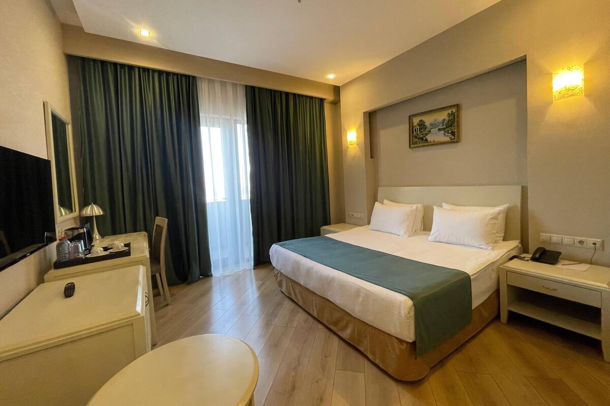 A hotel room with a bed, bedside table, chair, desk, and a television.