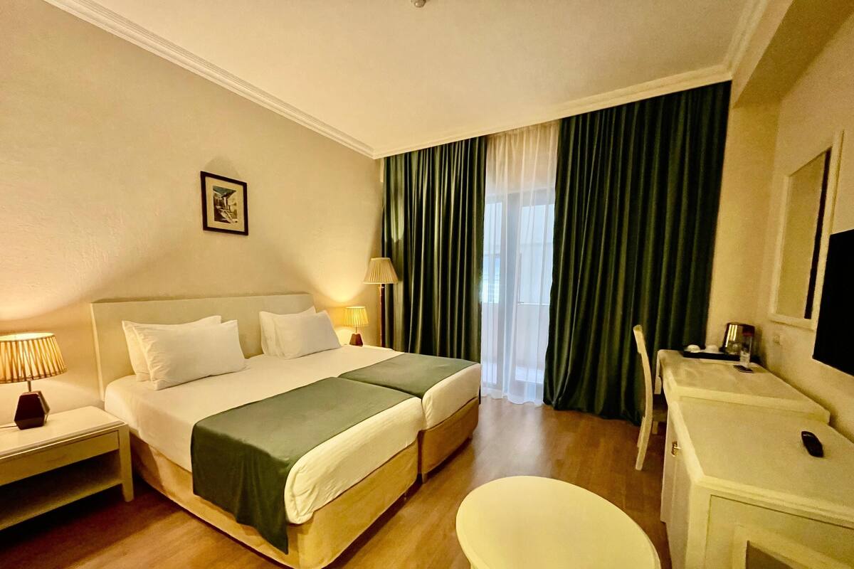 A hotel room with a bed, bedside tables, a desk, a chair, and a TV.