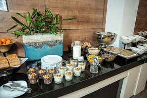A buffet with various food items, including cakes, pastries, and a plant centerpiece.