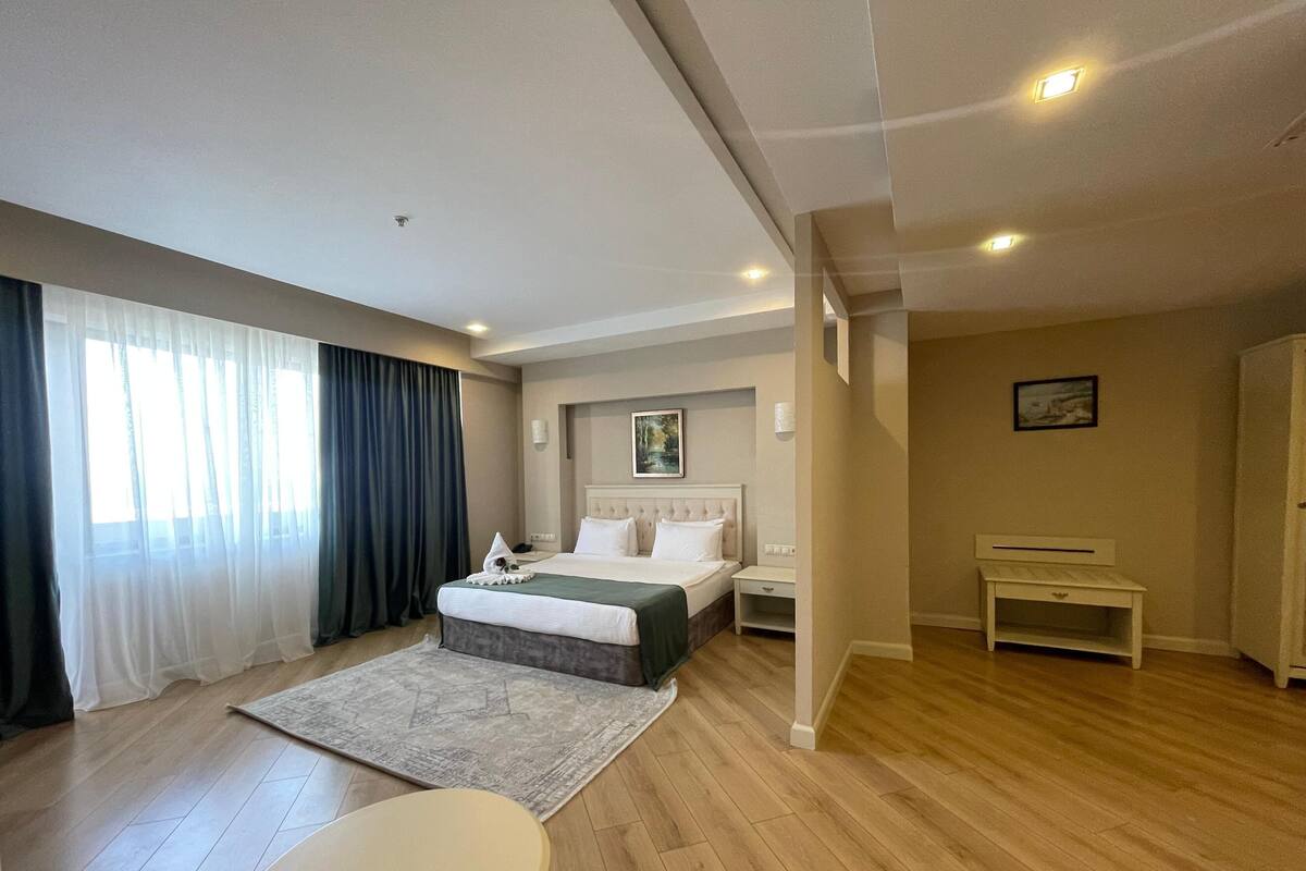 A hotel room with a bed, a bedside table, a chair, a small table, a rug, and a painting on the wall.