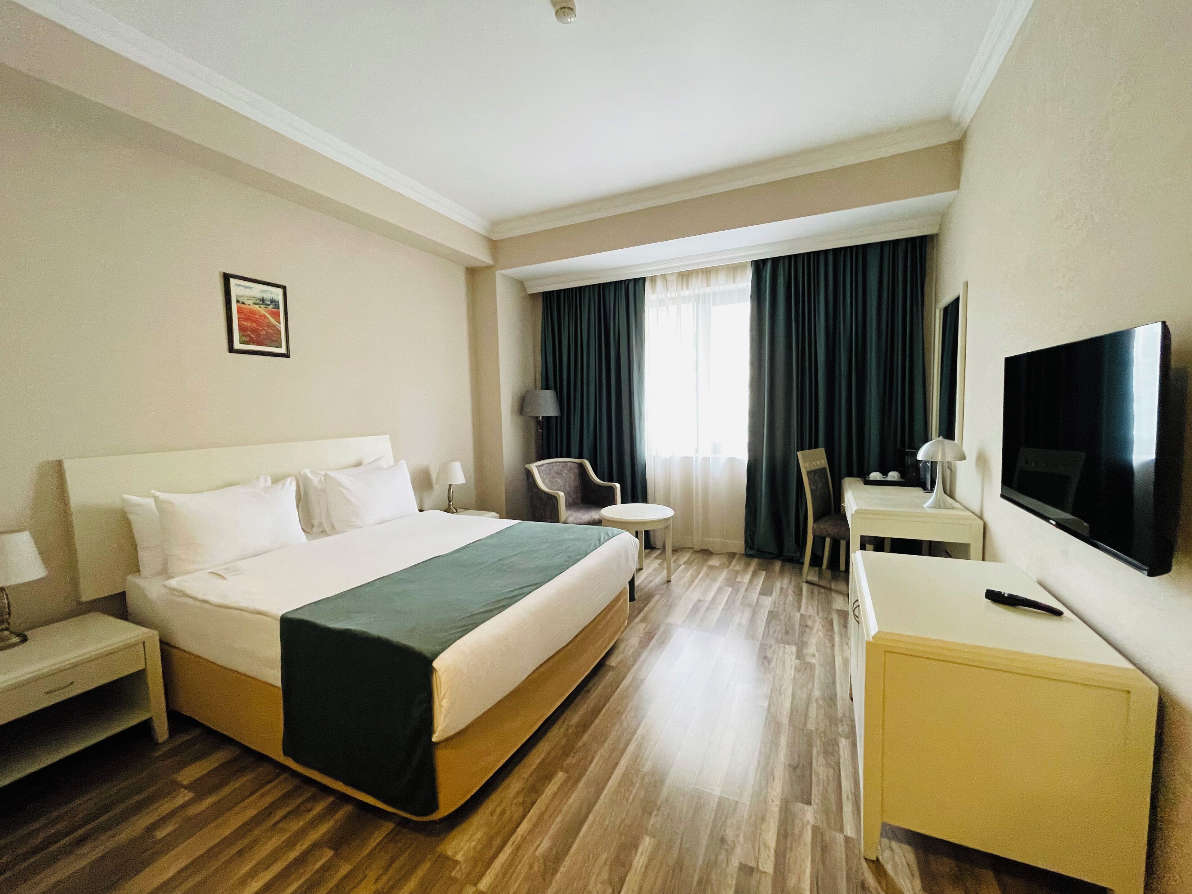 A hotel room with a bed, desk, chair, television, and a small table.