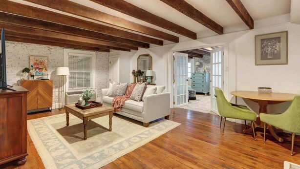 A spacious living room with wooden beams, a white sofa, a coffee table, and a dining area with green chairs. - The Quaint Quarters on Jones, Historic | Quiet (Savannah)