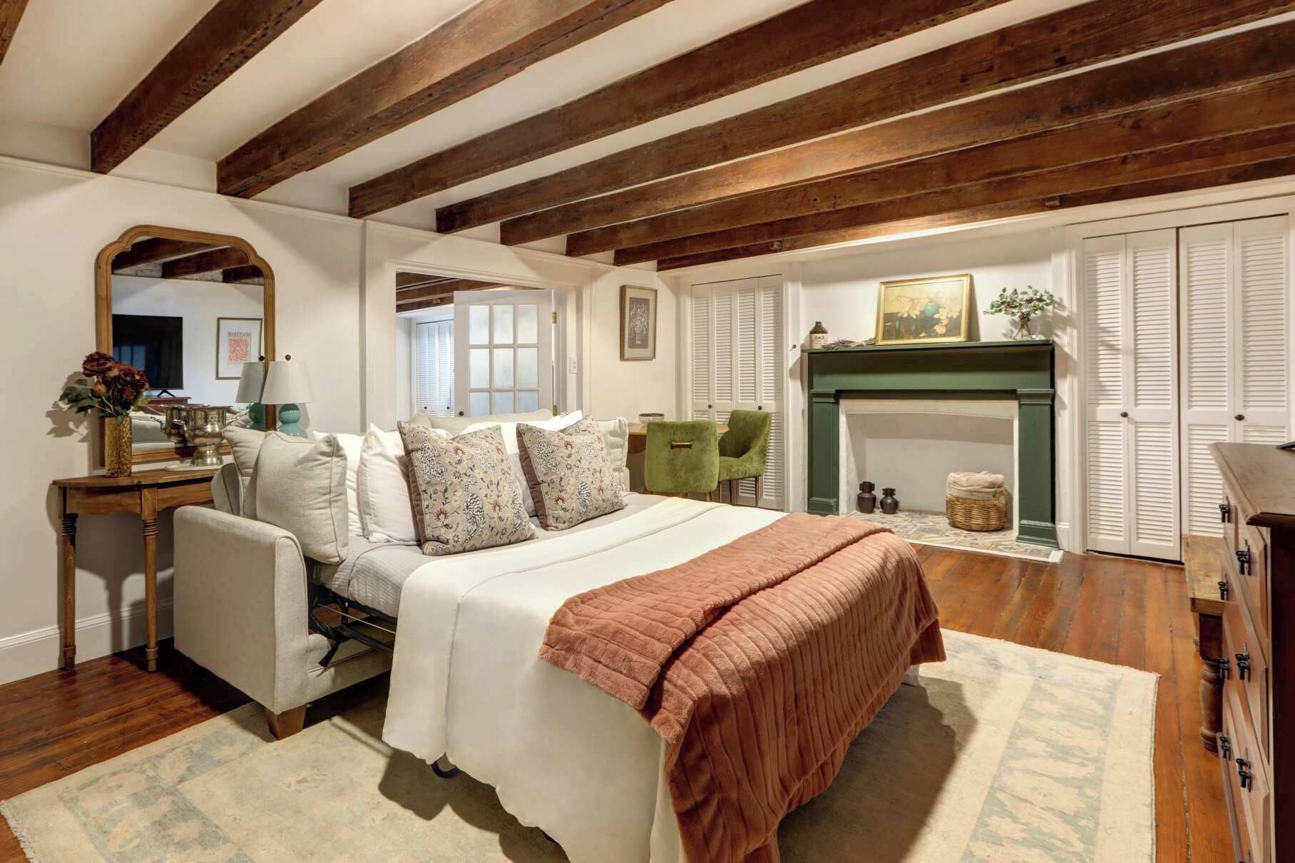 Een slaapkamer met een bed, een groene fauteuil, een open haard, een spiegel en een dressoir.