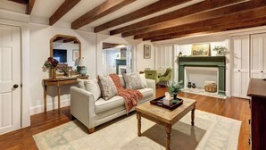 A living room with a white sofa, wooden beams, a fireplace, and a dining area. - The Quaint Quarters on Jones, Historic | Quiet (Savannah)