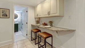 A kitchen with white cabinets, a granite countertop, two stools, and a door leading to a bathroom. - The Quaint Quarters on Jones, Historic | Quiet (Savannah)