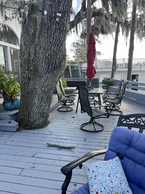 Una terraza de madera con mobiliario exterior, un árbol grande y una barandilla.