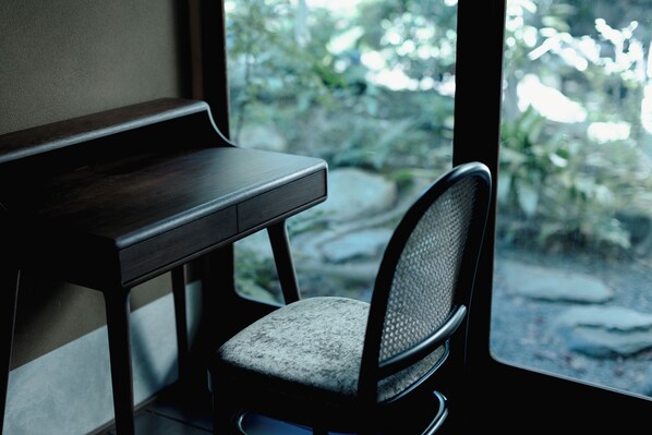 A wooden desk and a chair with a mesh backrest, positioned near a window with a view of rocks and greenery. - The Villa Higashiyama Roji Kazeno Heritage (Kyoto)