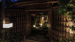 A traditional Japanese-style entrance with a wooden gate and a stone pathway leading to a lantern-lit garden.