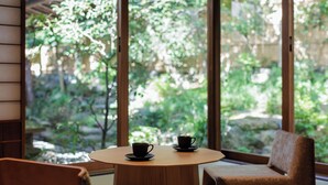 A round wooden table with two black cups on saucers, positioned near a window with a view of greenery.