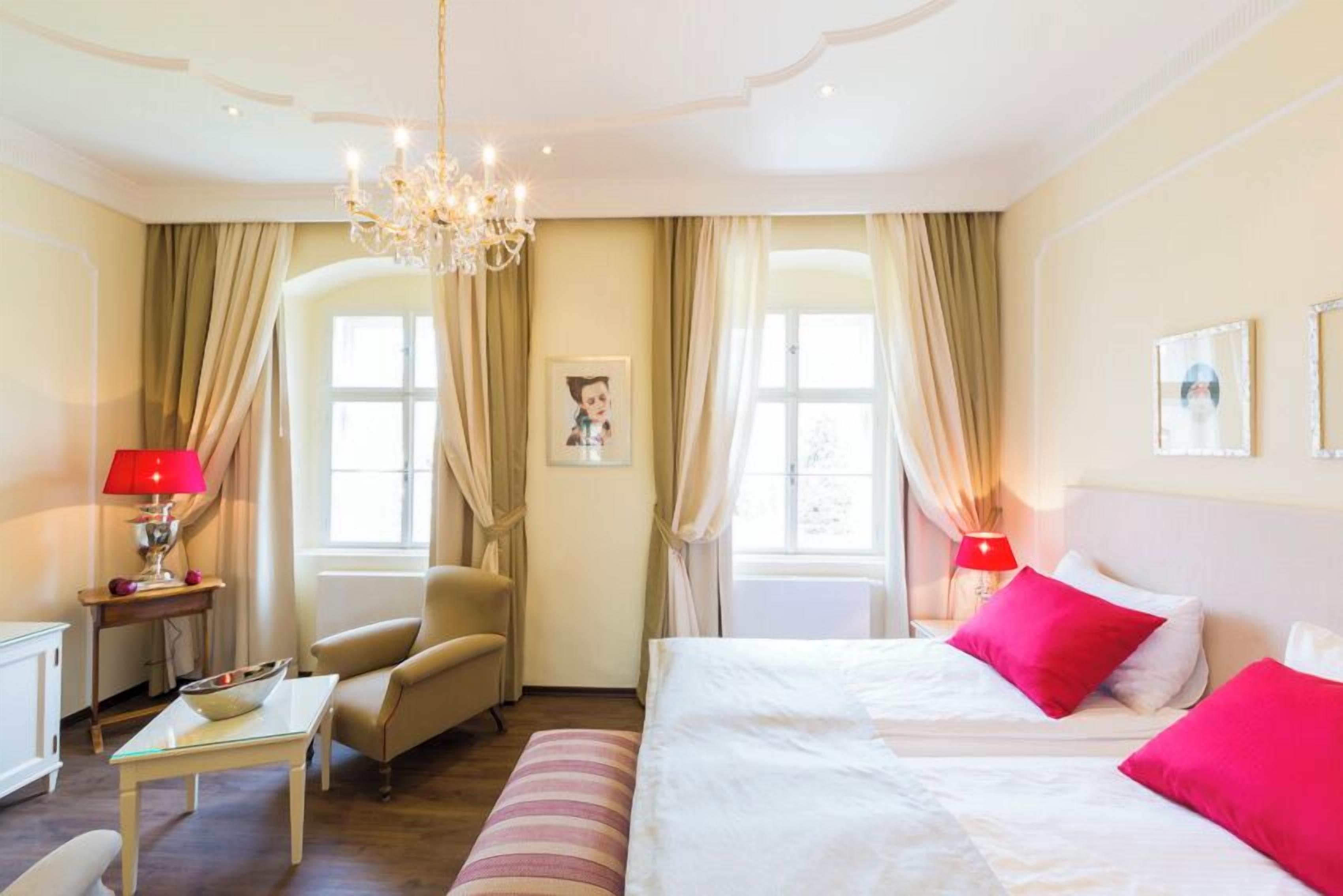 Una habitación de hotel con cama, una silla, una mesa, una araña y cortinas.