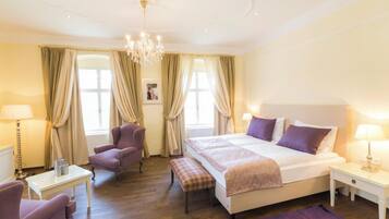A hotel room with a large bed, two armchairs, a small table, and a chandelier.