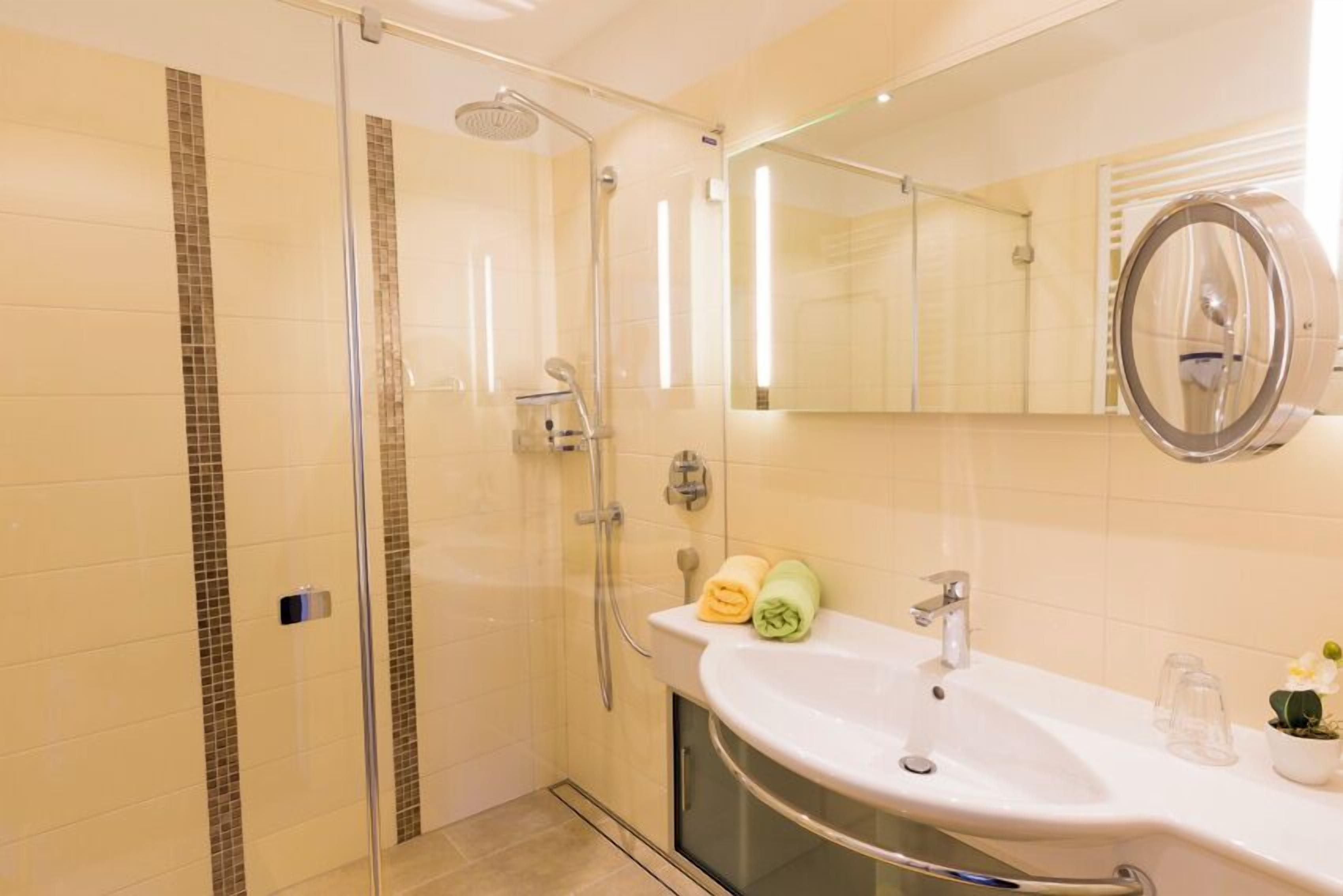 Un baño moderno con ducha envuelta en vidrio, un lavabo blanco y un espejo de marco redondo.