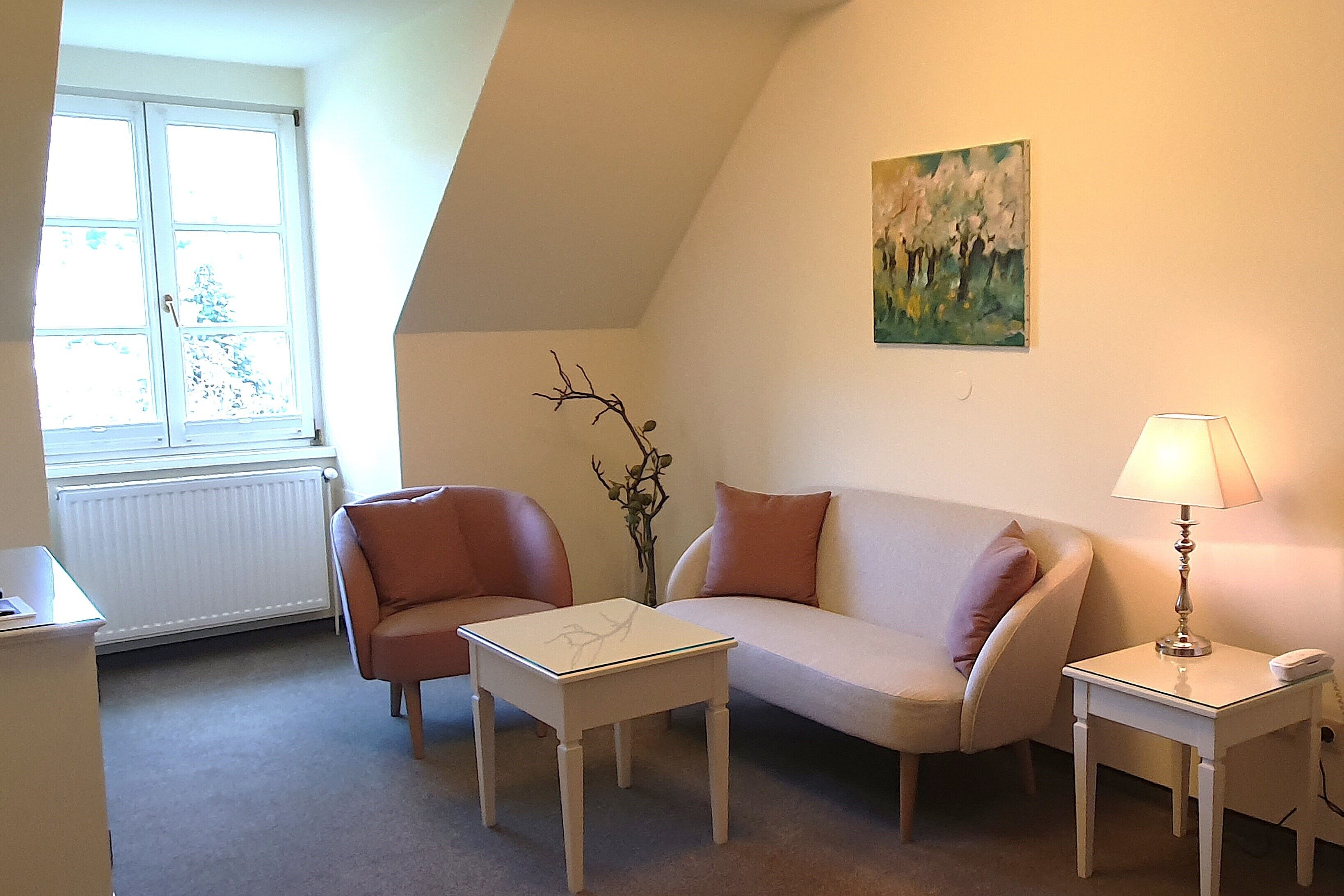 Ein gemütliches Wohnzimmer mit einem weißen Sofa, einem kleinen weißen Tisch, einer Lampe und einer Heizung.
