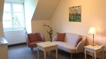 Ein gemütliches Wohnzimmer mit einem weißen Sofa, einem kleinen weißen Tisch, einer Lampe und einer Heizung.