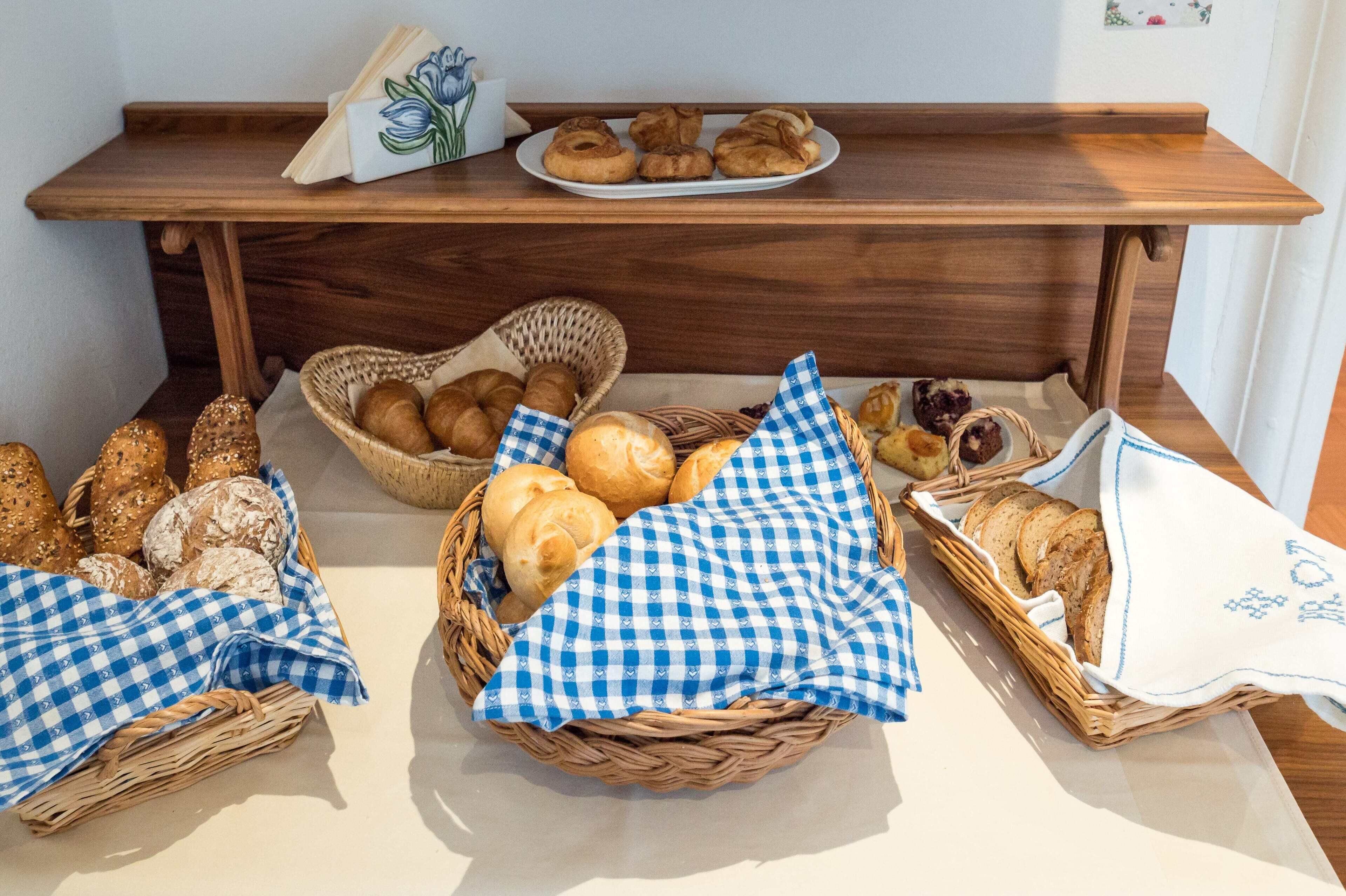 A buffet table with various breads and pastries in wicker baskets and cloths.