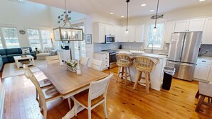 Une cuisine moderne avec des meubles blancs, des appareils en acier inoxydable et un coin repas comprenant une table en bois et des chaises en osier.
