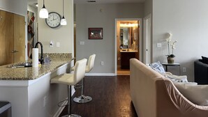 A modern kitchen with a granite countertop, white bar stools, and a hanging light fixture.