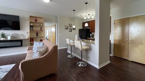 A modern living room with a sofa, a TV, and a kitchen area with bar stools.