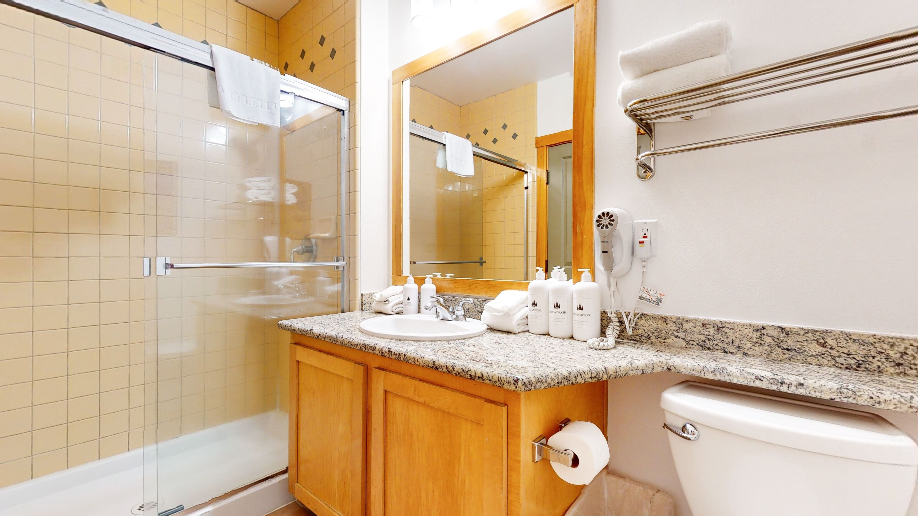 A bathroom with a glass-enclosed shower, a sink with toiletries, and a toilet.