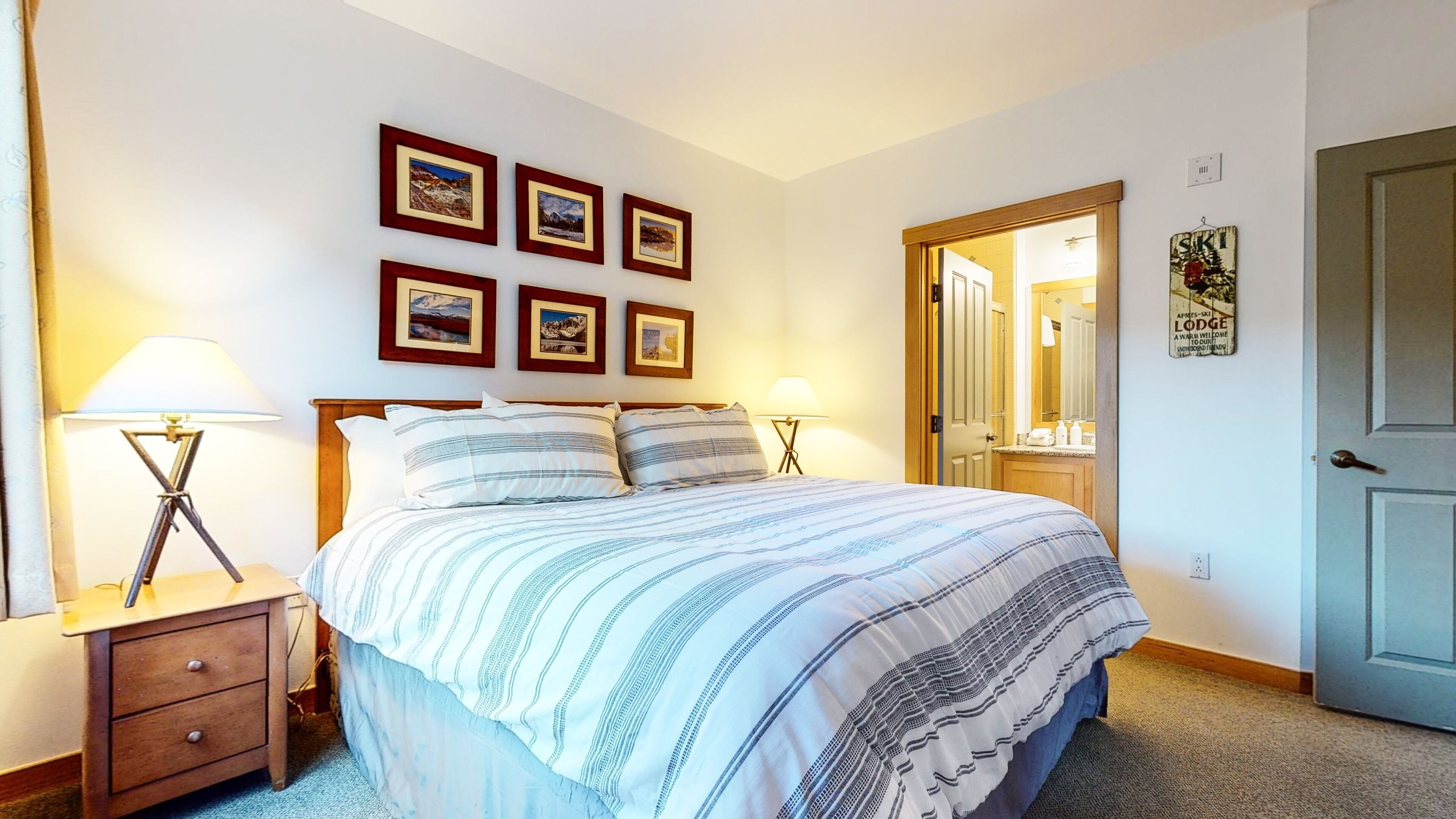 A bedroom with a bed, two bedside tables with lamps, a wooden headboard, and four framed pictures on the wall.