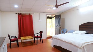 A bedroom with a bed, two chairs, a small table, and a door leading outside. - Vistara Resort (Araku Valley)