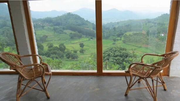 Two wicker chairs facing a large window with a view of green hills and mountains. - Vistara Resort (Araku Valley)