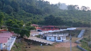 A rural setting with a small building with a red roof, surrounded by greenery and a white fence. - Vistara Resort (Araku Valley)