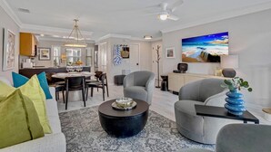 Un salon moderne comprenant un coin repas, un canapé gris, une table basse et un tableau représentant une scène de plage.