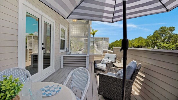 Une terrasse extérieure couverte, aménagée avec des meubles en osier, une table avec un plateau en verre et un parasol à rayures.