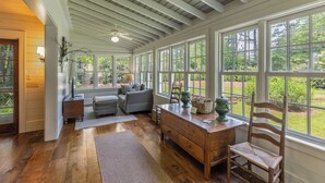 Une pièce spacieuse avec un plafond haut, de grandes fenêtres, un plancher en bois et un coin salon confortable avec un canapé et un fauteuil.