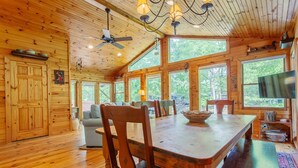 A wooden cabin interior with a dining table, chairs, a sofa, and a television. - Evans Cabin Creekside Cabin Rental (Bryson City)