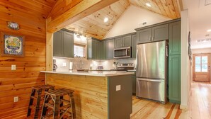 A kitchen with wooden walls, a central island, bar stools, a refrigerator, and a microwave. - Evans Cabin Creekside Cabin Rental (Bryson City)