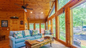 A cozy cabin interior with a blue sofa, wooden coffee table, and large windows offering a view of the outdoors. - Evans Cabin Creekside Cabin Rental (Bryson City)