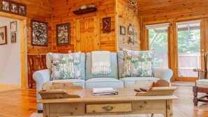 A cozy living room with a light blue sofa, patterned cushions, a wooden coffee table, and a rustic wooden ceiling. - Evans Cabin Creekside Cabin Rental (Bryson City)