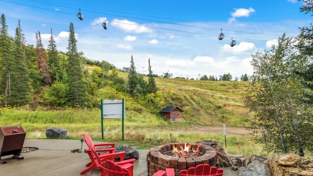 A patio with red Adirondack chairs, a fire pit, and a grill.