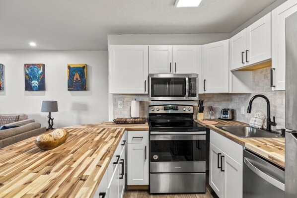 A modern kitchen with white cabinets, a stainless steel oven, a microwave, and a wooden countertop. - Remodeled 1-Bdrm Ski-In/Ski-Out Condo w/Mt Views! (Steamboat Springs)