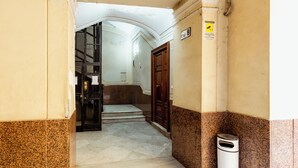 A hallway with a marble floor, a trash bin, a wooden door, and a sign with an emergency exit symbol. - Umberto I Residence (Napoli)