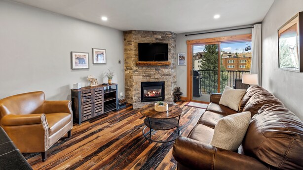Una sala de estar acogedora con chimenea de piedra, muebles de cuero y un ventanal con vistas a un balcón.