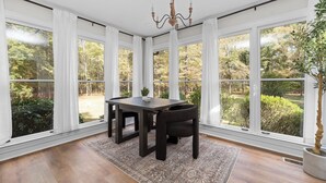 A dining room with a dark wooden table and chairs, large windows with white curtains, a chandelier, and a view of a garden. - Cozy/Luxe Winter Countryside Estate on Private Grounds in South CLT-King Suite!  (Marvin)