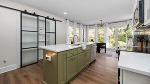 A modern kitchen with a large island, white cabinetry, and a sliding glass door leading to a garden. - Cozy/Luxe Winter Countryside Estate on Private Grounds in South CLT-King Suite!  (Marvin)