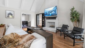 A modern living room with a fireplace, a television mounted on the wall, and a dining area visible through an open door. - Cozy/Luxe Winter Countryside Estate on Private Grounds in South CLT-King Suite!  (Marvin)