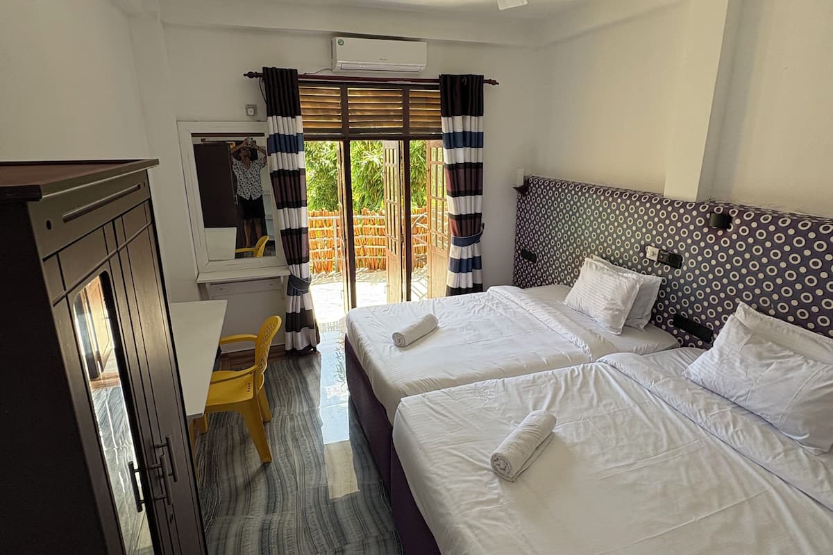 A hotel room with two beds, a desk, a chair, and a ceiling fan.