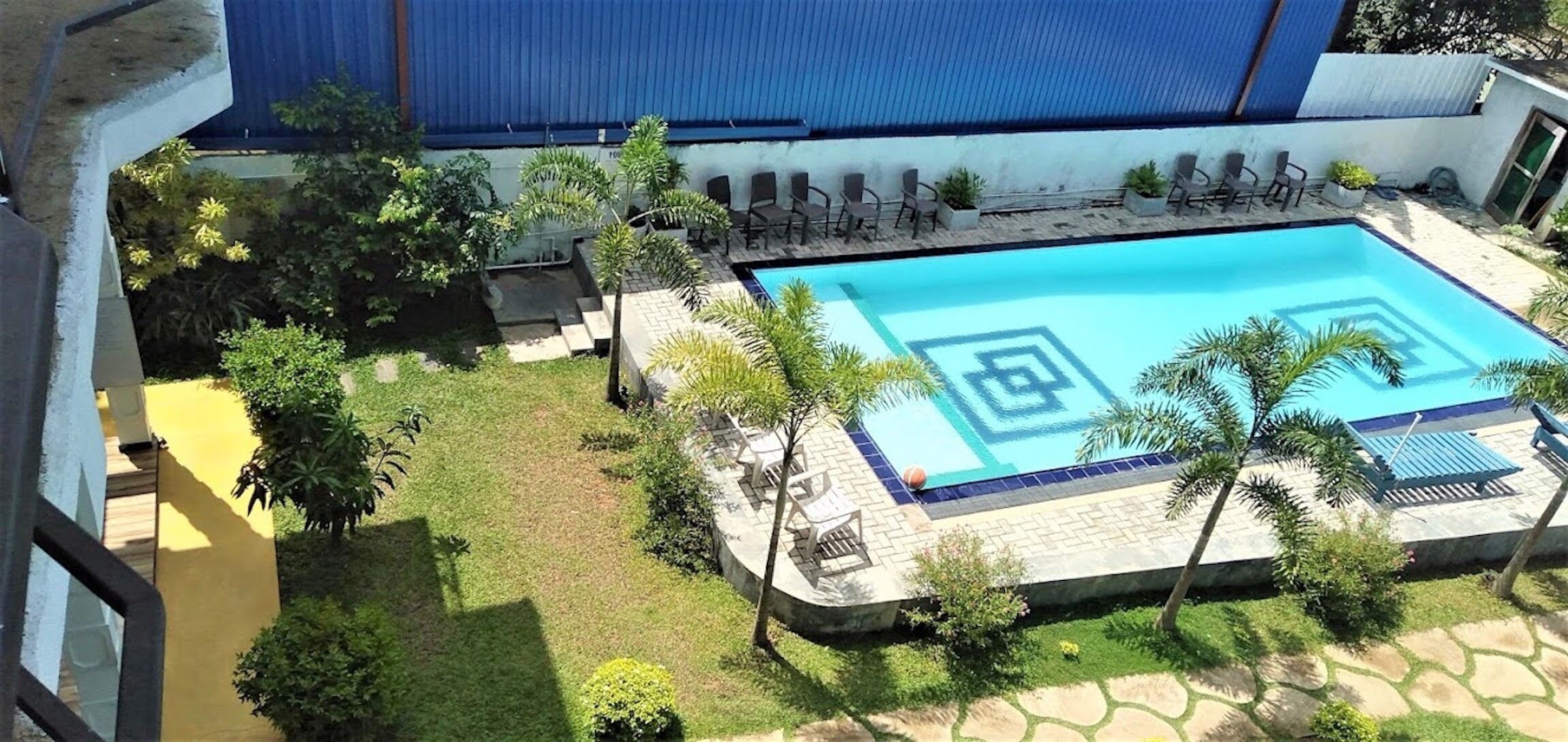 Una piscina con diseño geométrico, rodeada de sillas de descanso y palmeras.
