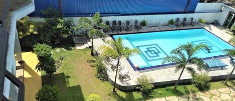 A swimming pool with a geometric pattern, surrounded by lounge chairs and palm trees.