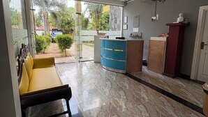A hotel lobby with a reception desk, a blue counter, a yellow sofa, and a ceiling fan. - Wake N Flow, Weligama - Coworking & Coliving (Weligama)