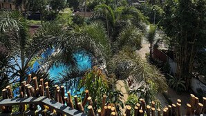 A pool surrounded by palm trees and tropical vegetation, with a wooden fence in the foreground. - Wake N Flow, Weligama - Coworking & Coliving (Weligama)